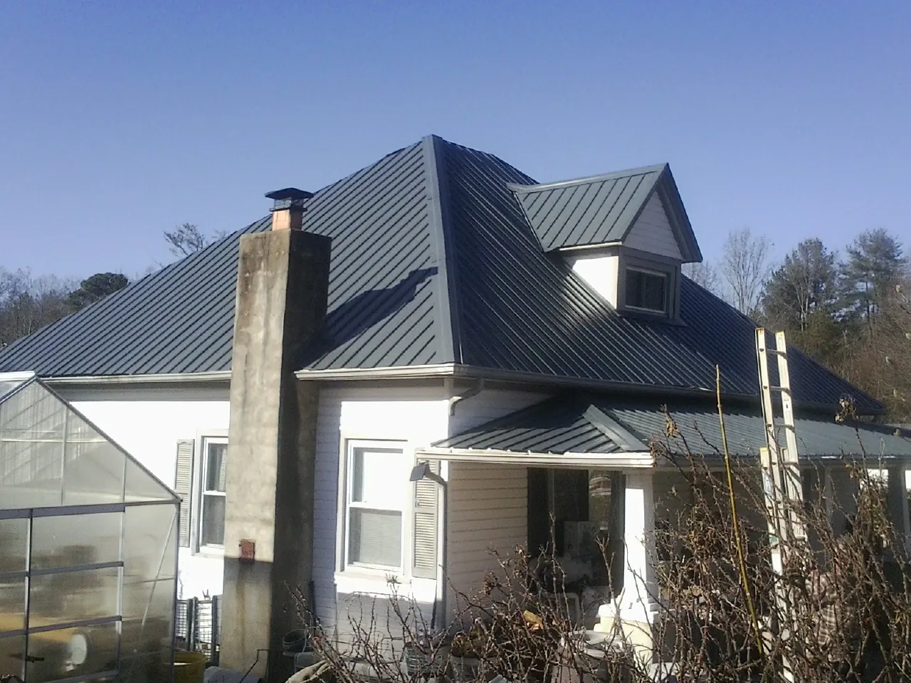 Dark blue standing seam metal roof on a white farmhouse with dormer — Slate & Tile Roof Repair by Roofing Brothers in Emerado