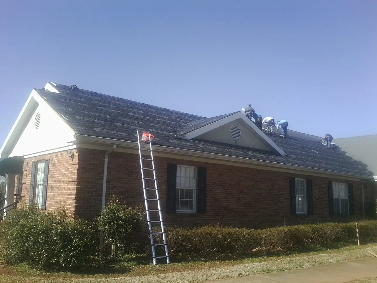 Crew tearing shingles off a brick ranch roof with a ladder set — Emergency Roof Repair work by our crew in Emerado
