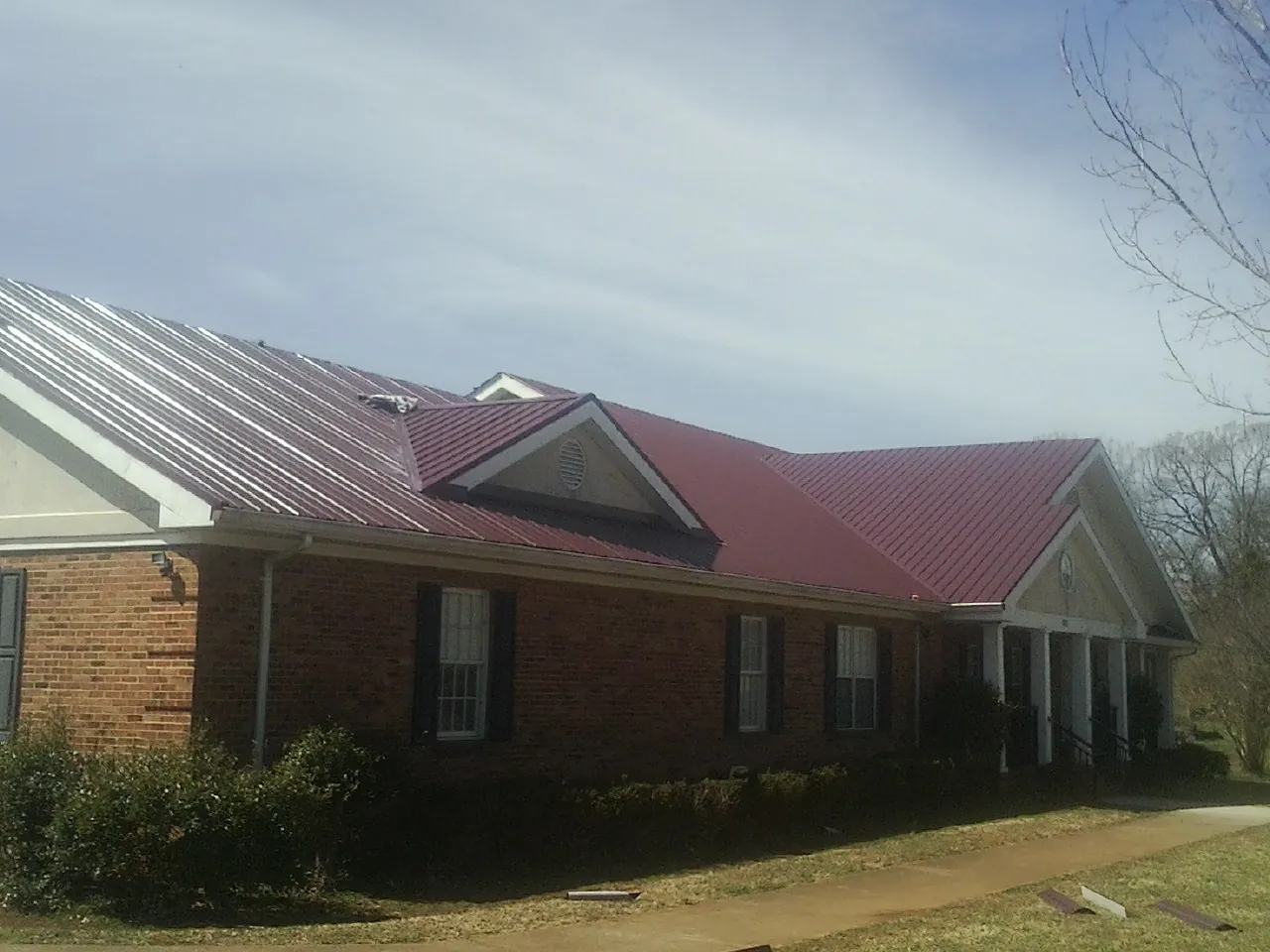Red metal roof with gabled entries on a long brick building, from a Hail Damage Roof Repair job in Emerado