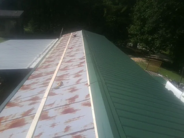 Old rusted panels beside newly installed green metal roofing — Wind Damage Roof Repair by Roofing Brothers in Emerado