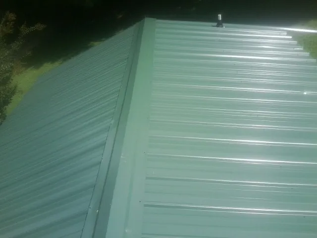 New green metal panels meeting at the ridge of a roof — Flat Roof Repair work by our crew in Emerado