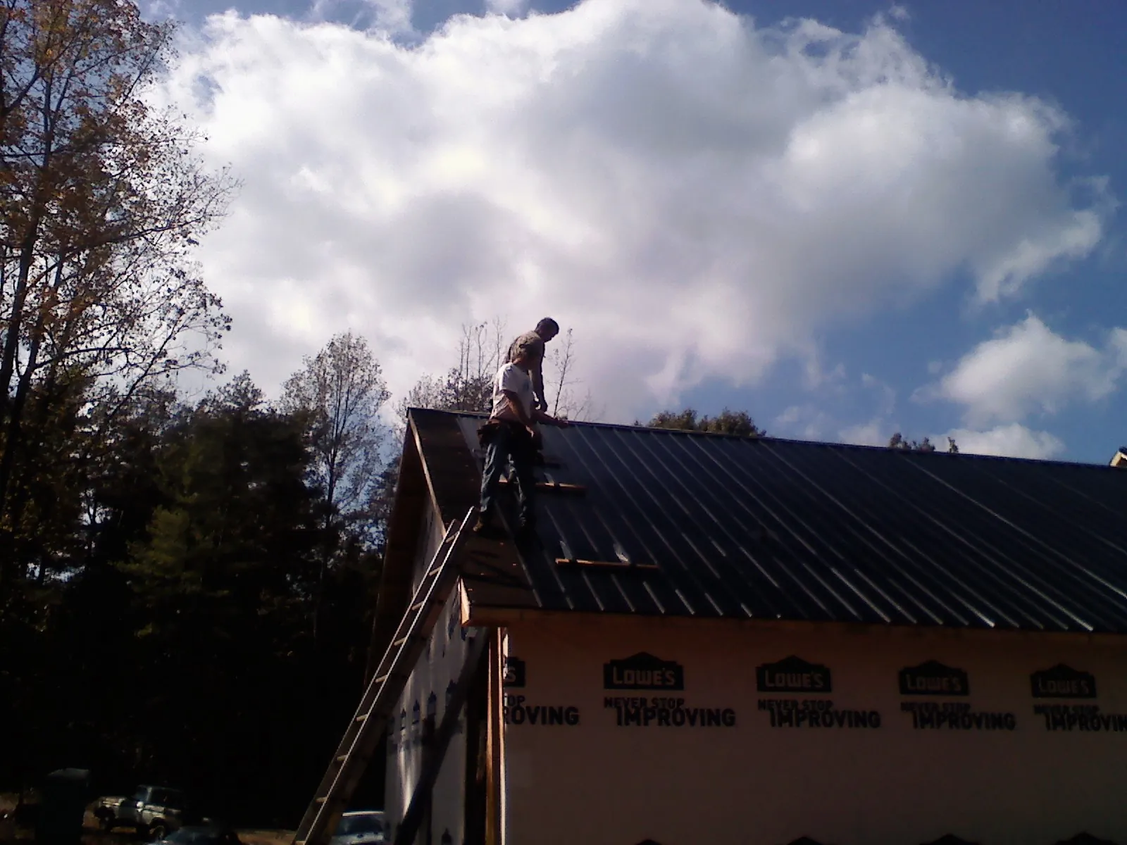Roofer fastening dark metal panels high against a cloudy sky, from a Roof Inspection job in Emerado