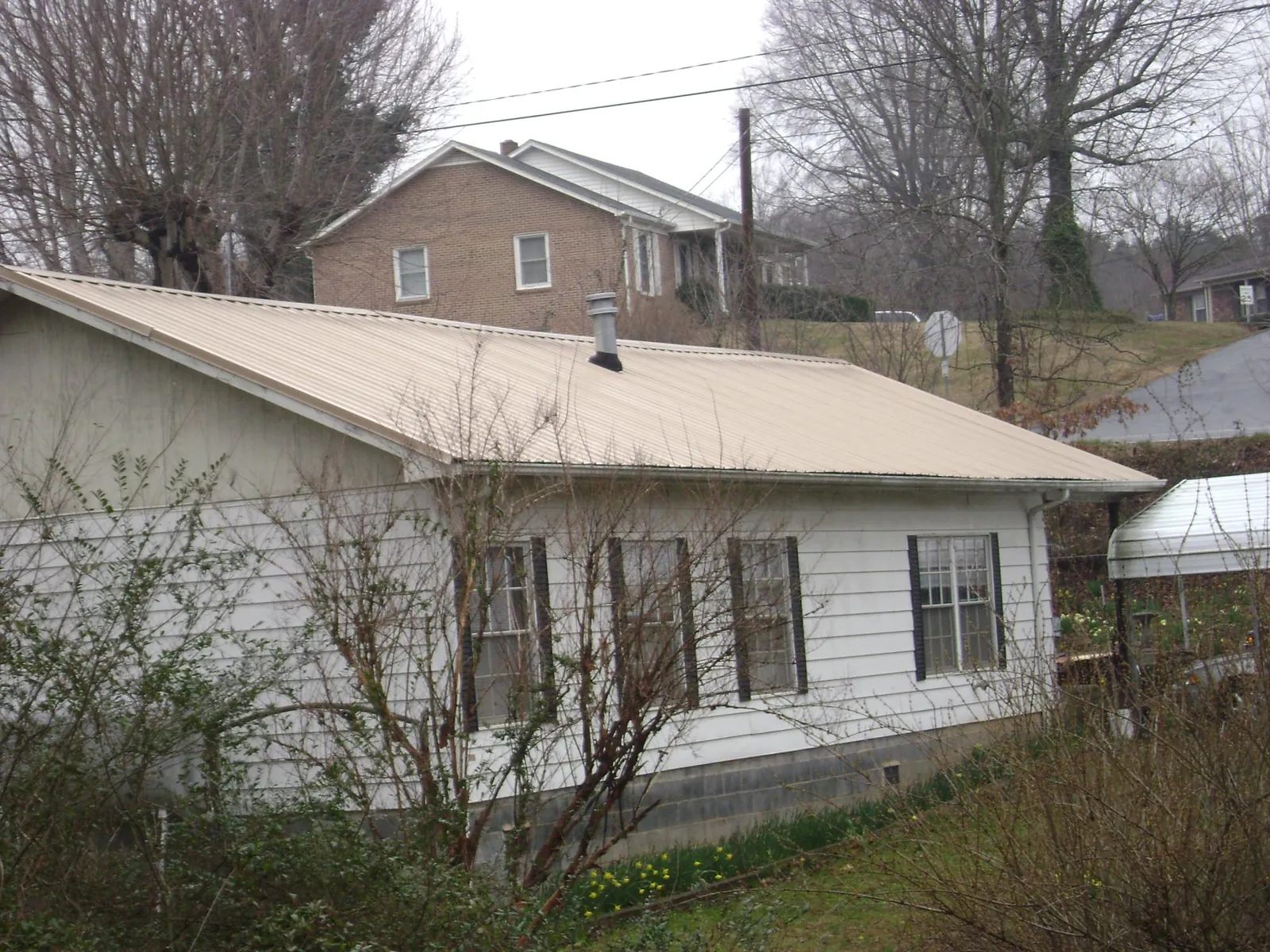 Tan metal roof on a white sided house set into a hillside — Commercial Roofing by Roofing Brothers in Emerado